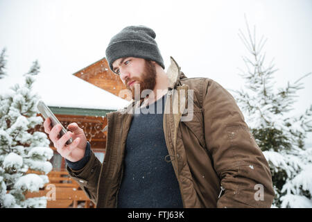 Serious bearded young man using smartphone standing outdoors in winter Stock Photo