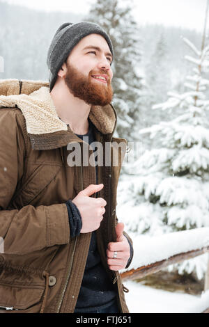 Smiling bearded young man standing in mountain winter forest Stock Photo