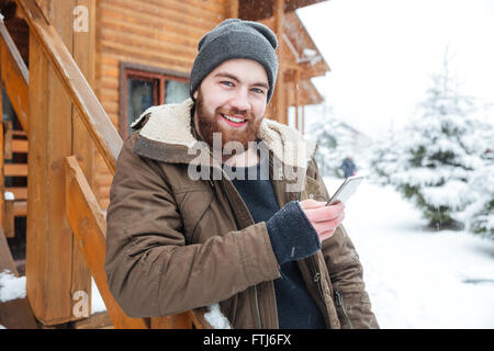 Cheerful bearded young man using smartphone outdoors in winter Stock Photo