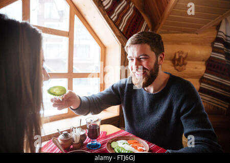 Happy young couple sitting at the table and eating together in wooden cottage Stock Photo