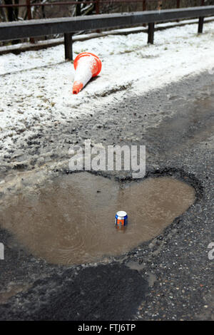 Large pothole on a Scottish road (A82) with a fizzy drinks can showing the depth of the hole Stock Photo