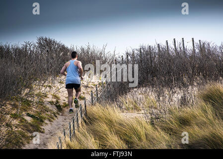 A man runs up a sand dune at Fistral Beach in Newquay, Cornwall. Stock Photo