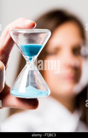 hourglass with a light blue sand flowing held by a woman (blurred) concerned about times that goes by Stock Photo