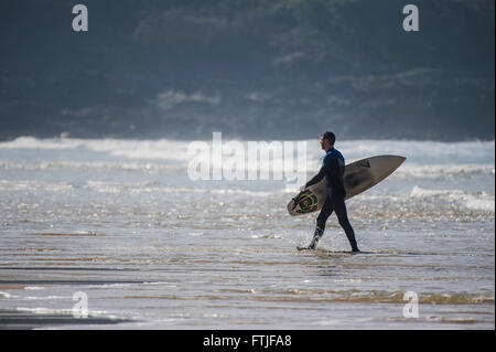 A surfer carries his surfboard as he walks out of the sea at Fistral Beach in Newquay, Cornwall. Stock Photo