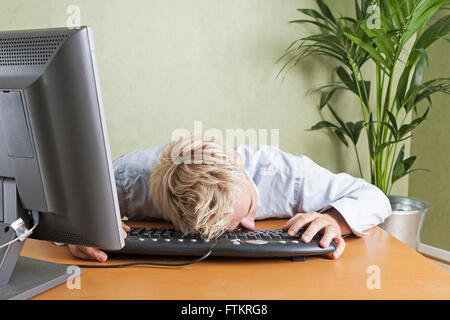 Tired man fallen asleep slumped over computer keyboard when working in office  Model Release: Yes.  Property Release: No. Stock Photo