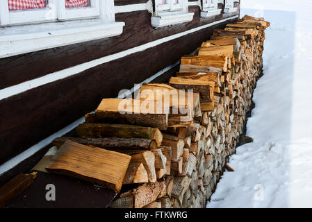 Windows of a traditional country cottage house with firewood logs during snowfall. Stock Photo