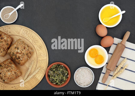 Pumpkin seed rolls on a wooden bread board with baking ingredients on slate background. Stock Photo