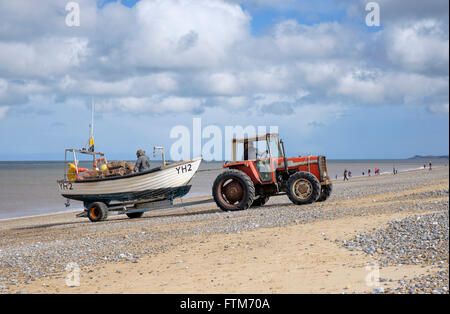 Tractor launching a crab/lobster fishing boat  to go inshore fishing near Cley Next The Sea, Norfolk, England, UK