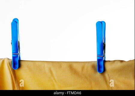 Blue plastic clothes peg or pin securing a yellow t-shirt on clothes line. Stock Photo