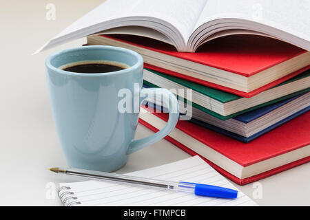 Student's study scene with pile of books and mug of strong black coffee by a notebook and pen on a desk for revising for exams. England UK Britain Stock Photo
