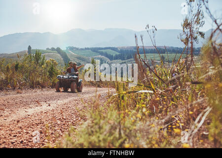 Young couple having fun on quad bike ride on a summer day. Young man driving the ATV girlfriend pointing at something interestin Stock Photo