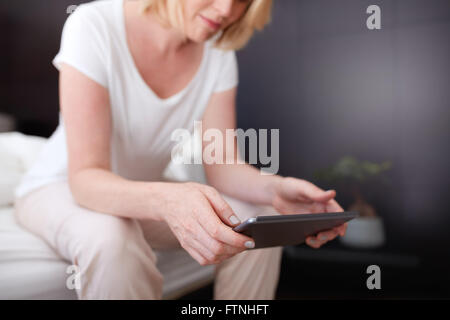 Cropped shot of a woman using digital tablet while sitting on the edge of bed. Focus on tablet  pc and woman hands. Stock Photo