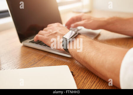Close up image of man with a smartwatch working on laptop while sitting at his desk. Stock Photo