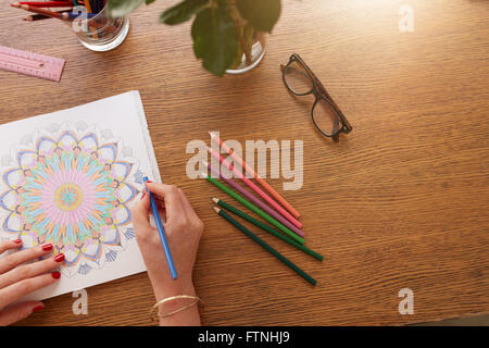 Close up image of female hands drawing in adult colouring book on a table at home. Stock Photo