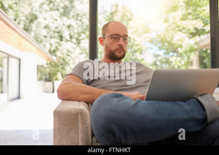 Portrait of mature caucasian man sitting on a sofa and working on laptop. Man surfing internet on laptop computer. Stock Photo