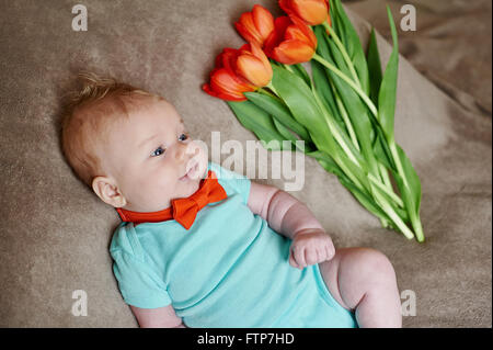 Little boy lying on the bed with a bouquet of tulips Stock Photo
