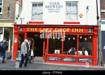 Men walking past The Last Drop Inn, with group of people sitting inside seen through window, Colliergate, York, Yorkshire Stock Photo