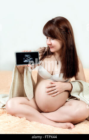 Portrait of pregnant woman holding phone with ultrasound photo of her belly on it Stock Photo