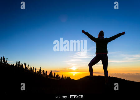 Woman hiker silhouette with arms outstretched in mountains. Female runner or climber looking at sunset view. Business concept an Stock Photo