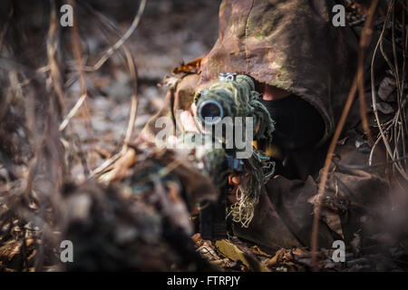 Sniper wearing camouflage suit with rifle hide in the woods Stock Photo