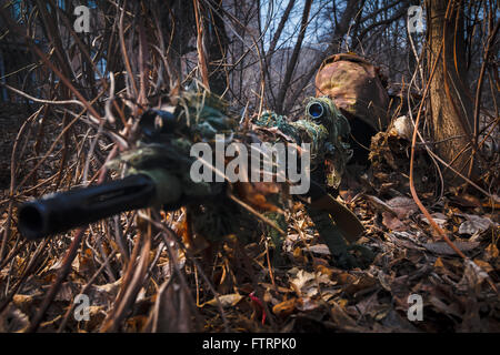 Sniper wearing camouflage suit with rifle hide in the woods Stock Photo