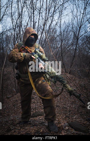Sniper wearing camouflage suit with rifle walk in the woods Stock Photo