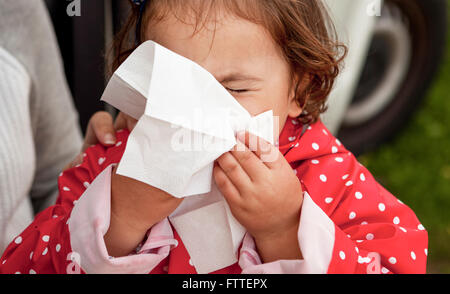 Baby girl dressed with dotted raincoat blowing her nose close to her mother Stock Photo