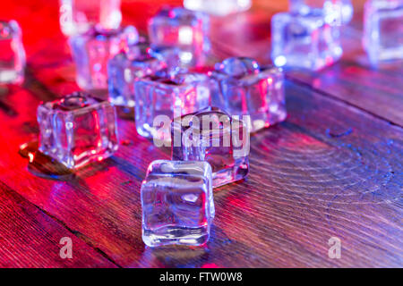 Cold and wet ice cubes with colorful light on wooden table Stock Photo