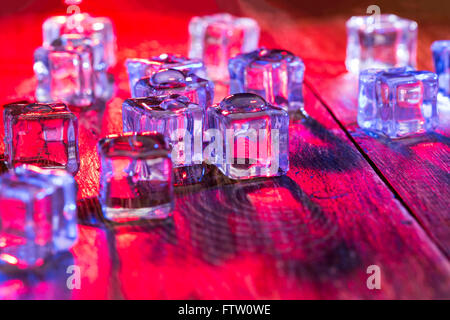 Cold and wet ice cubes with colorful light on wooden table Stock Photo
