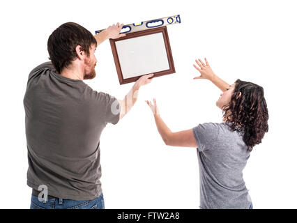 Photograph of a young man and young woman isolated on white. The man holds a picture frame and level which is clearly crooked wh Stock Photo