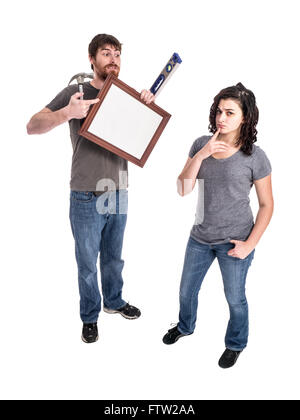 Photograph of a young man and young woman isolated on white. The man holds a picture frame and tools while the woman decides whe Stock Photo