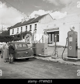 1950s, historical, at a rural petrol station/garage in the West of Ireland, a young lad filling up a lady's car, possibly a British-made Austin, with fuel. Stock Photo