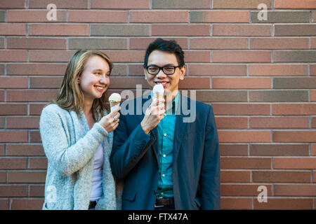 Two smiling young people holding ice cream cones standing near brick wall and chatting Stock Photo