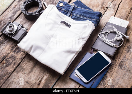 Woman travelling stuff on wooden background. Smartphone with black screen and clothes with camera arranged on the desk Stock Photo