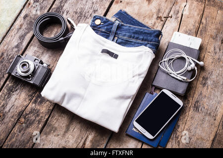 Woman travelling stuff on wooden background. Smartphone with black screen and clothes with camera arranged on the desk Stock Photo
