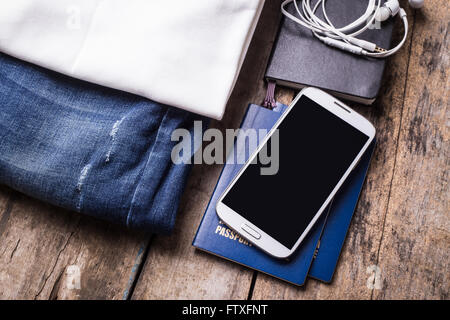 Woman travelling stuff on wooden background. Smartphone with black screen and clothes arranged on the desk Stock Photo