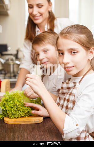 Happy family cooking background. Teenage sister and brother help their mother with cooking salad in the kitchen Stock Photo