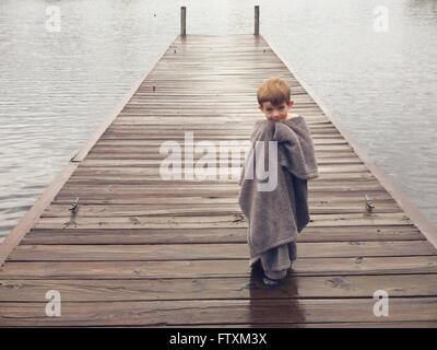 Boy wrapped in blanket, standing on pier Stock Photo