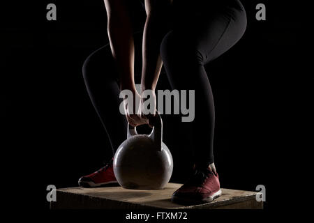Young woman standing on wooden box lifting kettlebell weights in gym Stock Photo