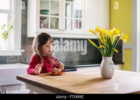 Girl sitting at a kitchen table eating a slice of chocolate cake Stock Photo