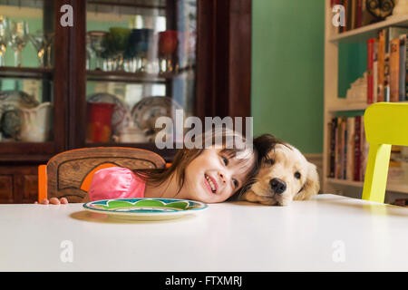 Girl sitting at table with golden retriever puppy dog Stock Photo