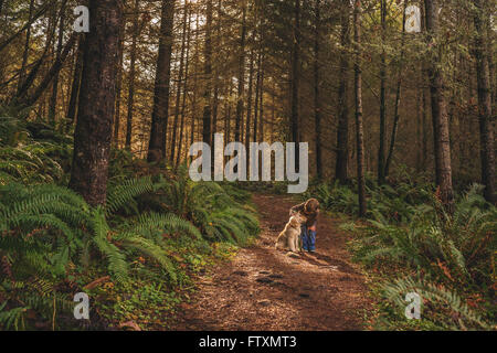 Boy stroking golden retriever puppy dog in forest Stock Photo