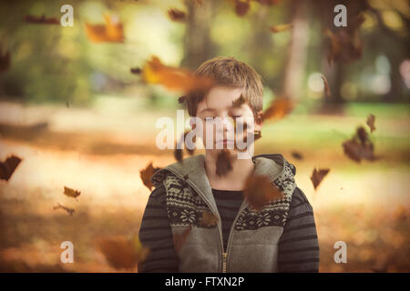 Boy standing in park with autumn leaves falling, Bulgaria Stock Photo