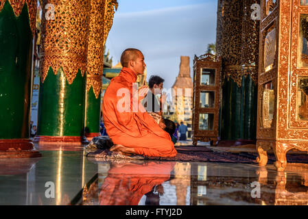 Asian monk prays  in the Shwedagon Pagoda Temple at sunset. Stock Photo