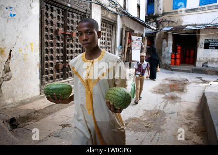 Man with a two water melons next to the massive teak doors of one house in Stone Town s maze of narrow streets, Zanzibar, Tanzan Stock Photo