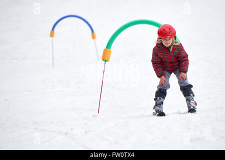 Child skiing in the mountains. Girl with safety helmet learning to ski at school. Winter sport for family with young children. Stock Photo