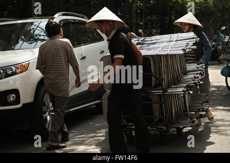 Young vietnamese people with traditional conical hat transporting chairs in the old city of Hanoi, Vietnam Stock Photo
