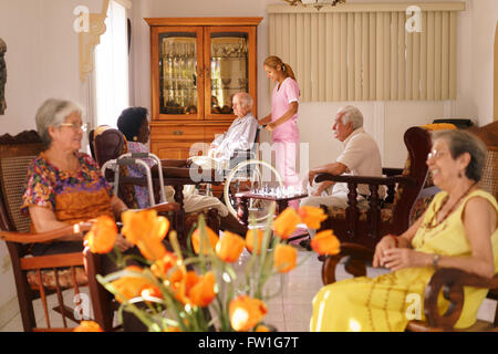 Old people in geriatric hospice: young attractive hispanic woman working as nurse helps a senior man on wheelchair. Stock Photo