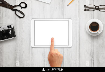 Hand touch tablet with isolated white screen for mockup. Work desk with camera, glasses, coffee, notepad and pencil beside Stock Photo