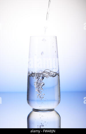 Water pouring into half-filled drinking glass with reflection on white and blue background Stock Photo